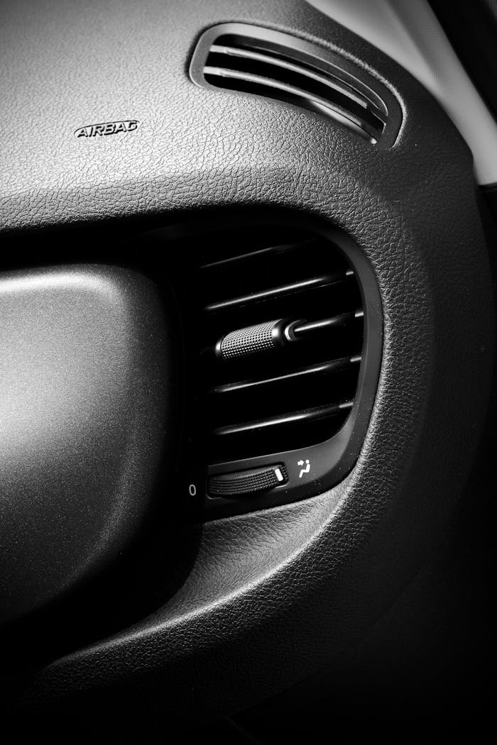 High detail image of a car's interior showing a black air conditioning vent on the dashboard.